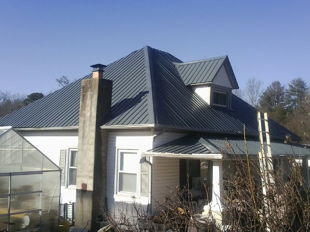 Dark blue standing seam metal roof on a white farmhouse with dormer — Slate & Tile Roof Repair by Roofing Brothers in Eaton Center