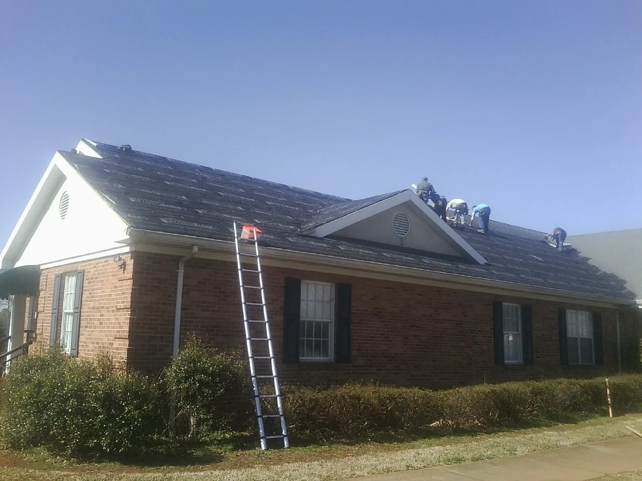 Crew tearing shingles off a brick ranch roof with a ladder set — Emergency Roof Repair work by our crew in Eaton Center