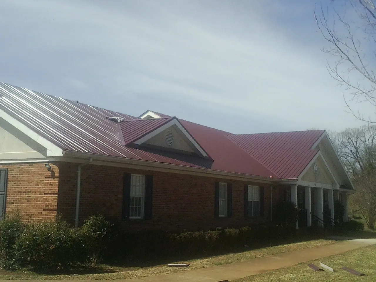 Red metal roof with gabled entries on a long brick building, from a Hail Damage Roof Repair job in Eaton Center