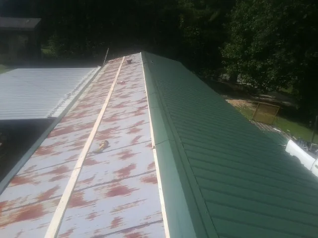 Old rusted panels beside newly installed green metal roofing — Wind Damage Roof Repair by Roofing Brothers in Eaton Center