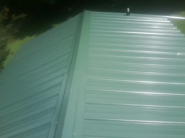 New green metal panels meeting at the ridge of a roof — Flat Roof Repair work by our crew in Eaton Center