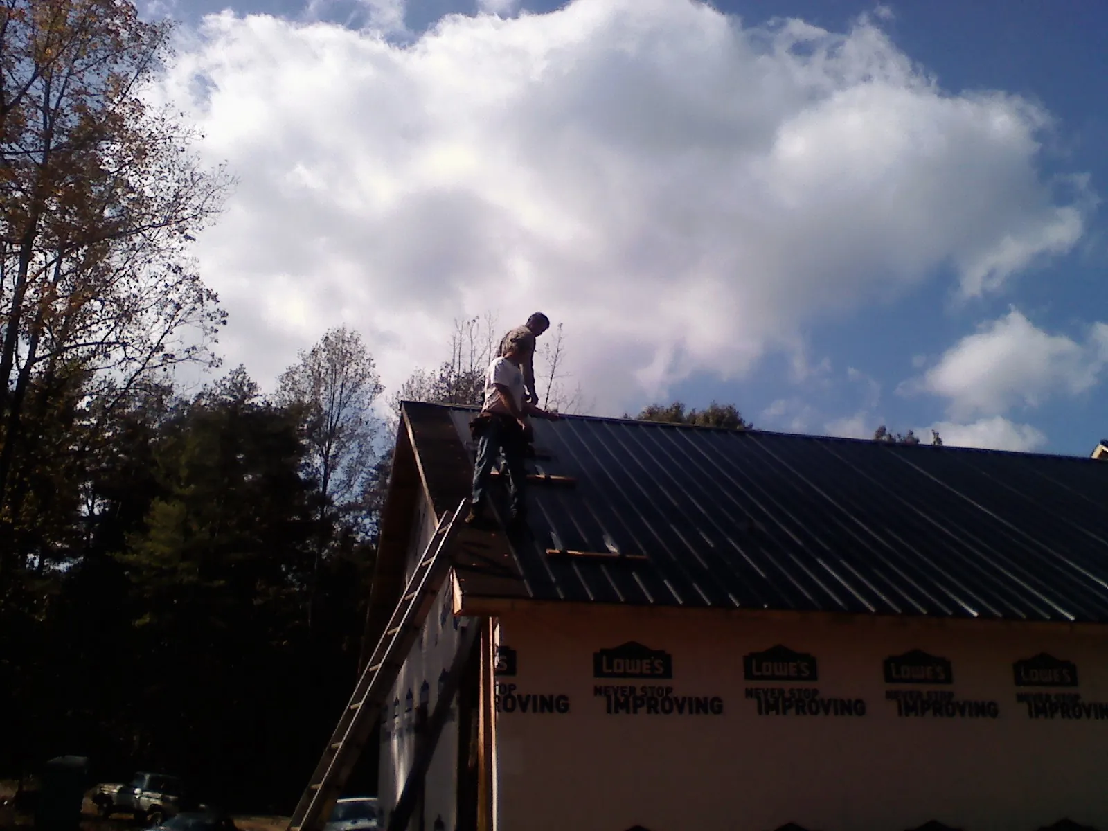 Roofer fastening dark metal panels high against a cloudy sky, from a Roof Inspection job in Eaton Center