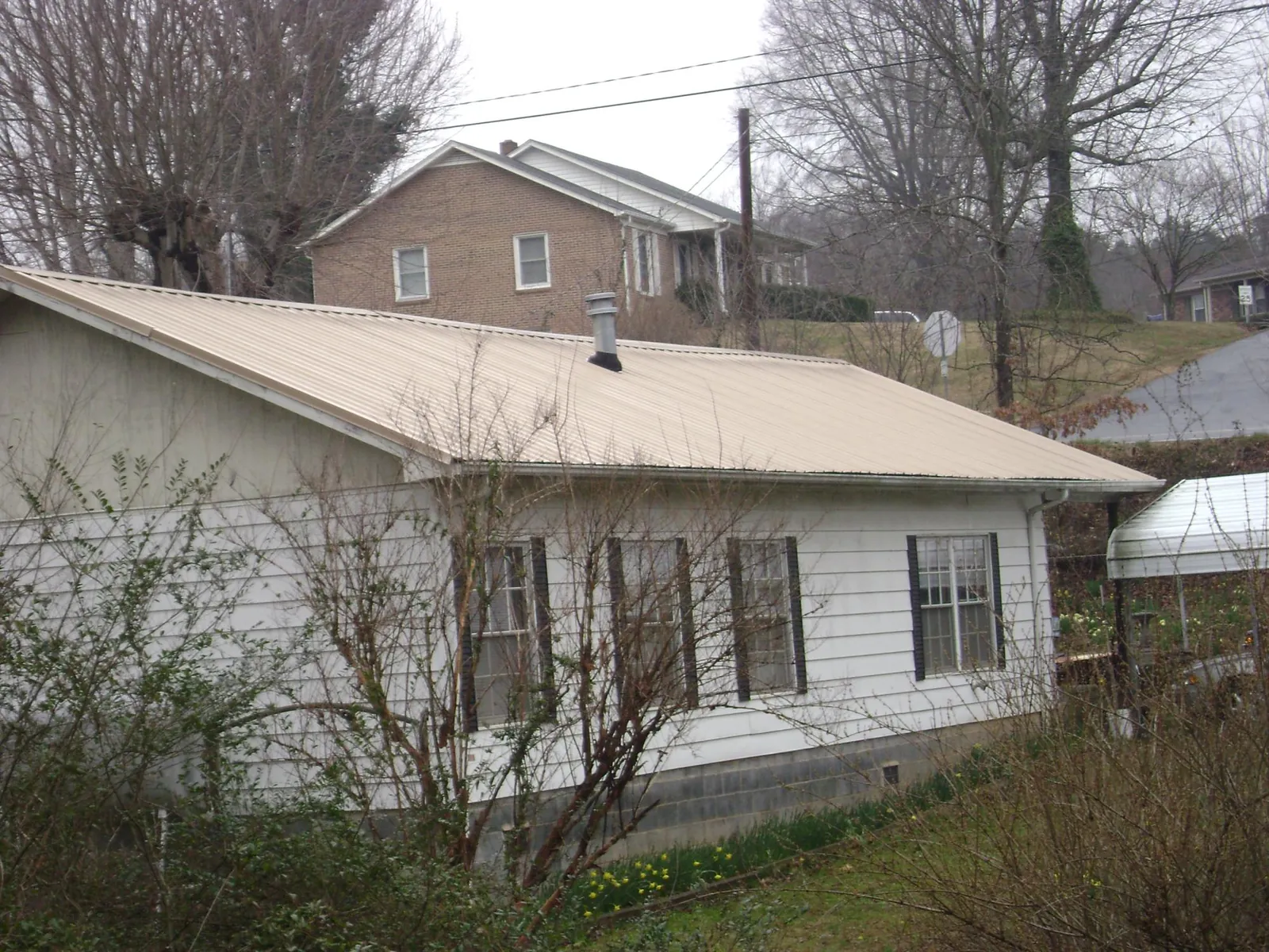 Tan metal roof on a white sided house set into a hillside — Commercial Roofing by Roofing Brothers in Eaton Center